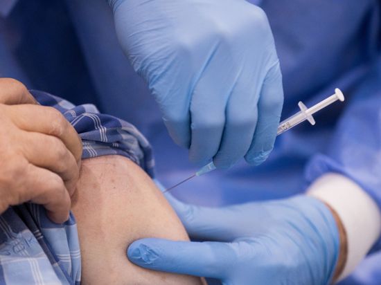 Ein Arzt impft einen Mann in einem Impfzentrum gegen Corona.