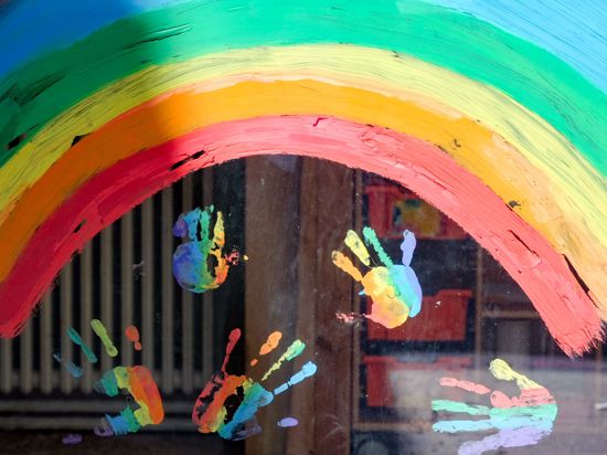 Kinderhände und ein Regenbogen sind an einer Kita zu sehen.