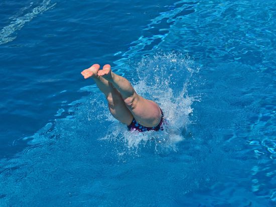 Eine Frau springt in einem Freibad ins Wasser.