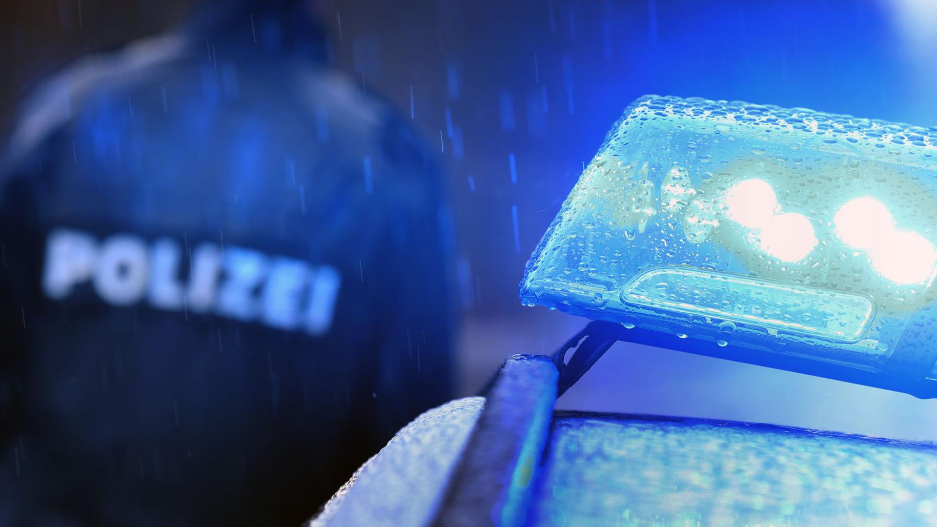 Ein Polizist steht vor einem Streifenwagen mit Blaulicht.