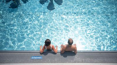 Zwei Badegäste stehen in einem Freibad im Schwimmbecken.