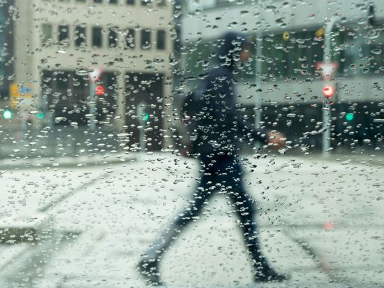 Regentropfen sammeln sich auf einer Autscheibe an der ein Mann vorbeigeht.