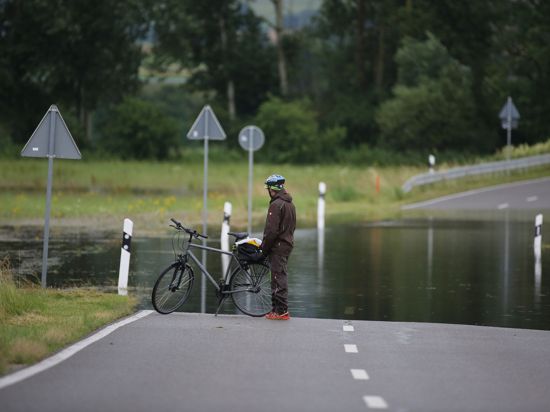 Ein Radfahrer steht an einer überfluteten Straße.