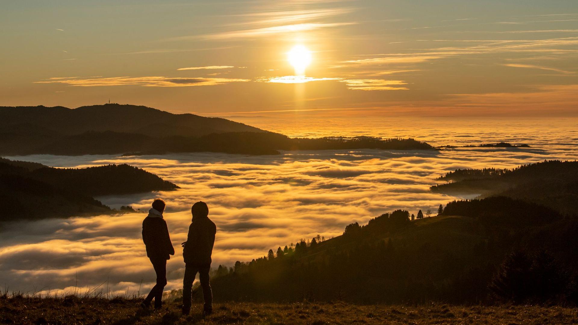 Zwei Spaziergänger betrachten den Sonnenuntergang über dem Wolkenmeer.