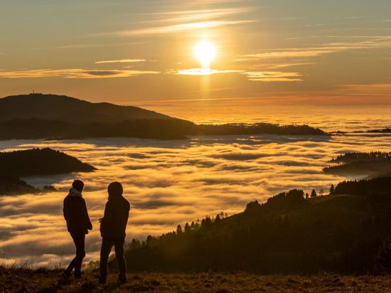 Zwei Spaziergänger betrachten den Sonnenuntergang über dem Wolkenmeer.
