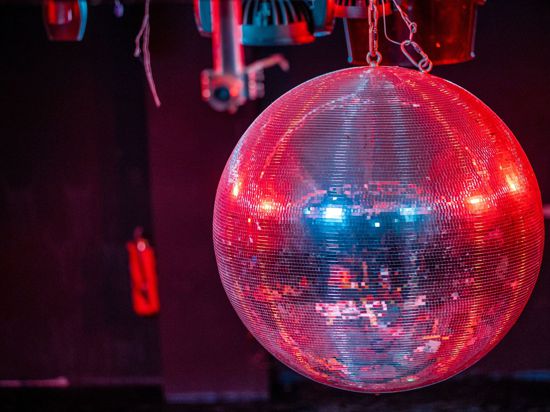 Eine farbig beleuchtete Discokugel dreht sich über der Tanzfläche in einer Diskothek.