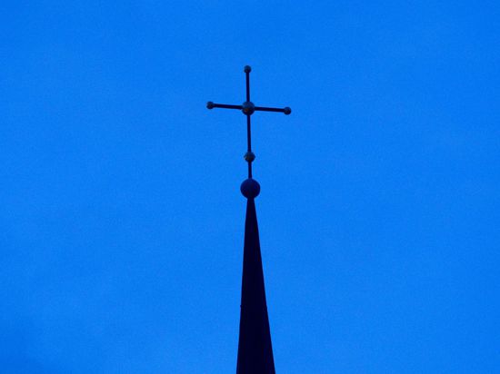 Das Kreuz einer Kirche ist in der Abenddämmerung zu sehen.