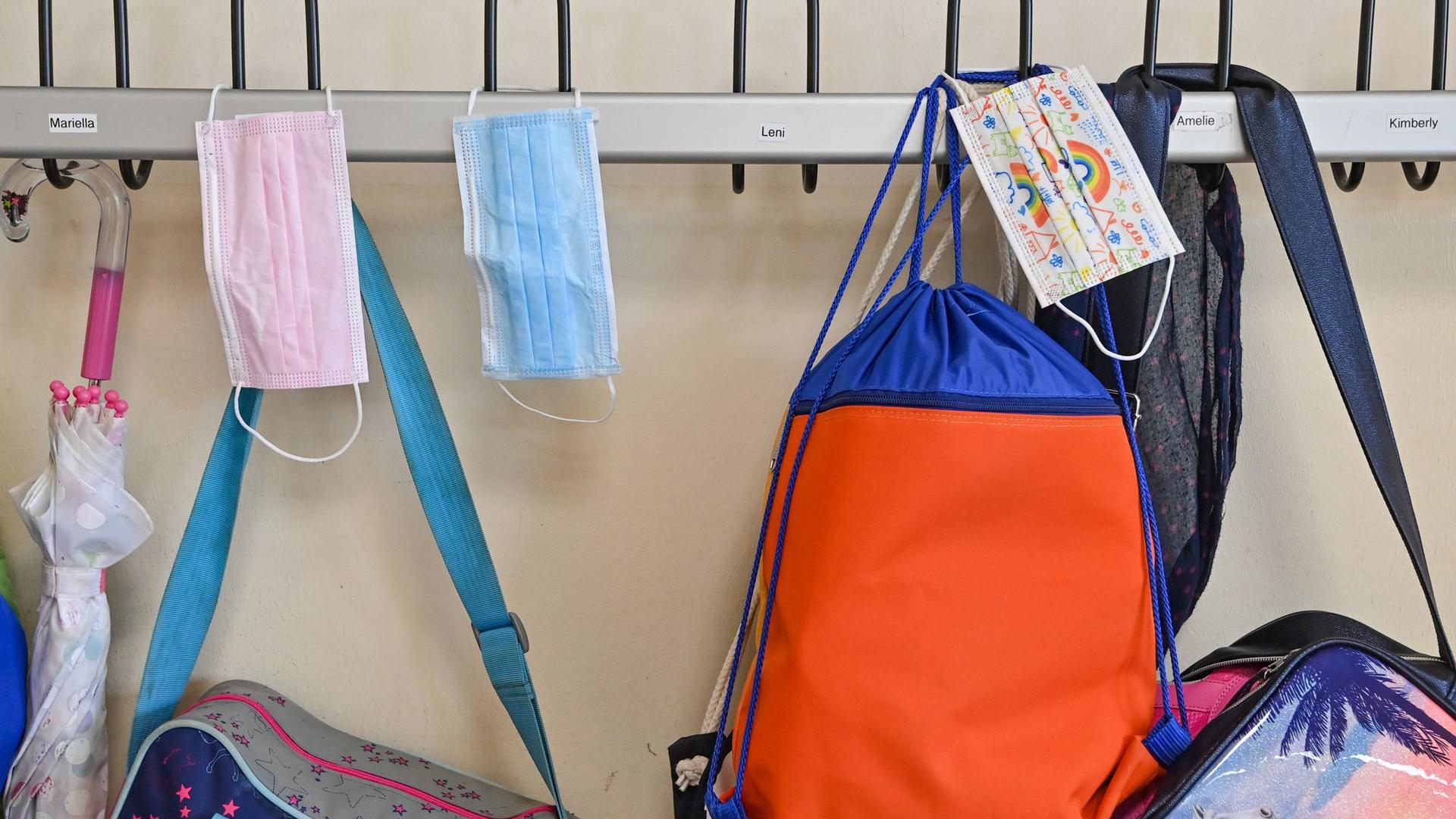 Masken und Taschen hängen in einer Grundschule an Kleiderhaken.