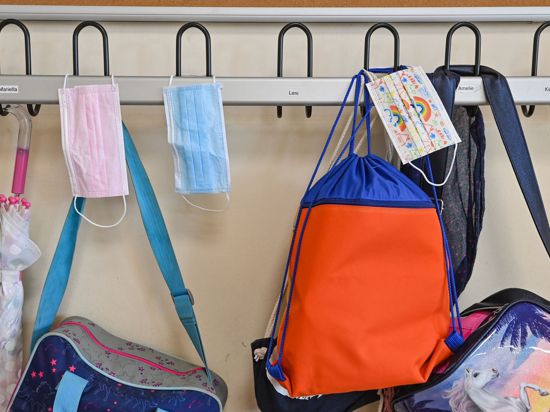 Masken und Taschen hängen in einer Grundschule an Kleiderhaken.
