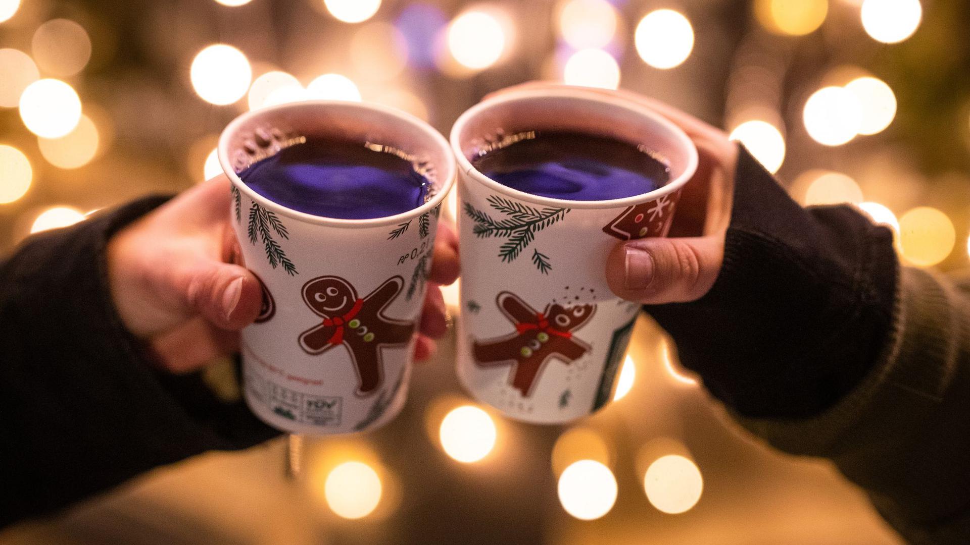 Zwei Besucherinnen eines Weihnachtsmarktes stoßen mit Glühwein an.