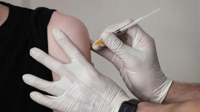 Ein Hausarzt impft einen Jugendlichen in seiner Praxis.