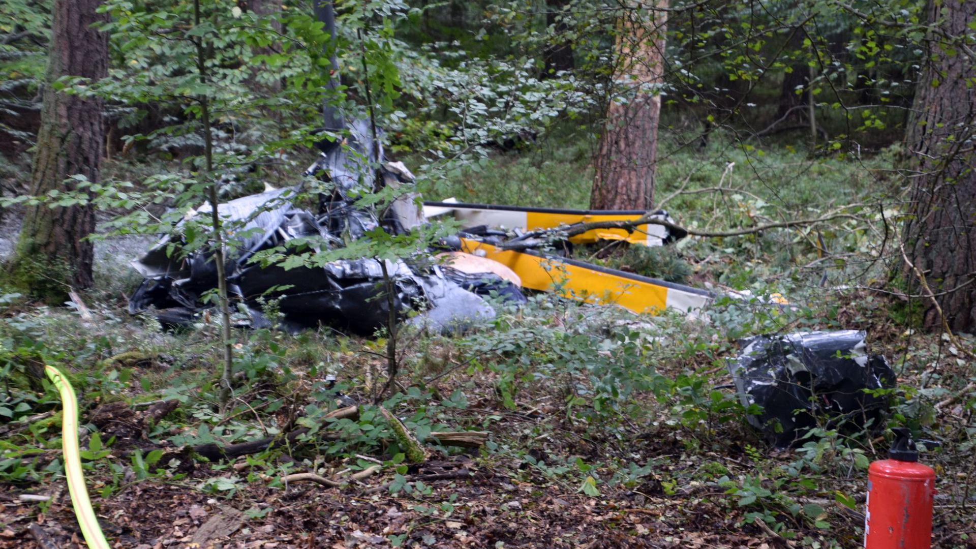 Trümmerteile eines Hubschraubers vom Typ Robinson R44 liegen in einem Wald.