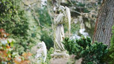 Zwei Engel stehen als Grabzierde auf einem Friedhof.