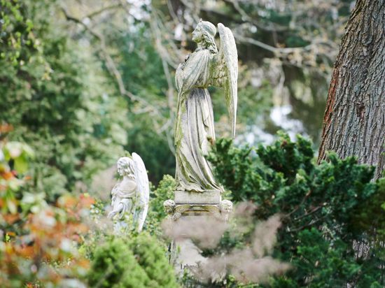 Zwei Engel stehen als Grabzierde auf einem Friedhof.