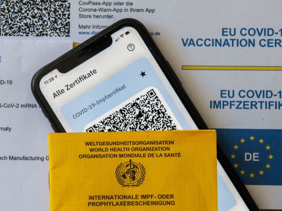 Ein Impfpass und ein Smartphone mit der CovPass-App liegen auf einem Impfzertifikat.