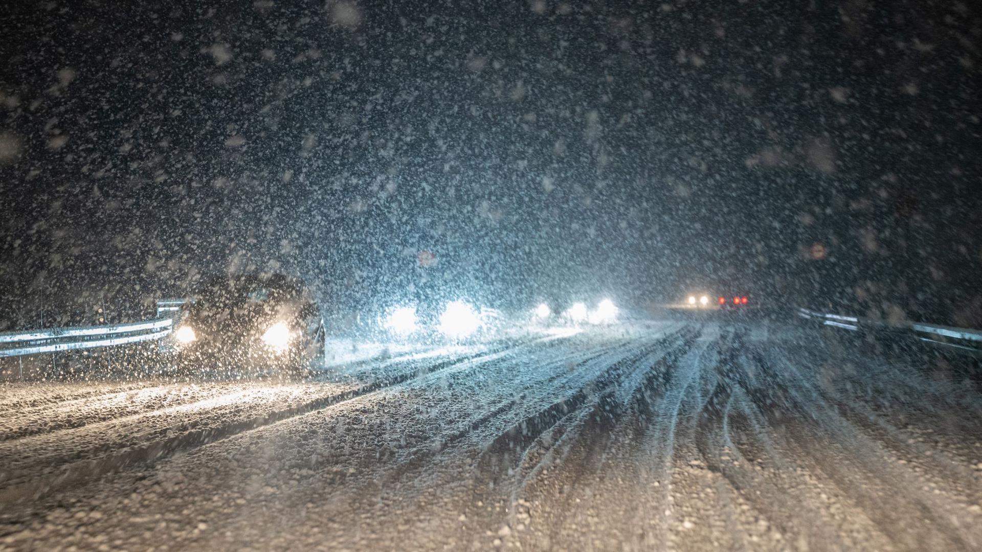 Im dichten Schneetreiben fahren Autos auf einer schneebedeckten Straße.