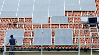 Ein Arbeiter installiert auf einem Dach eine Solaranlage.