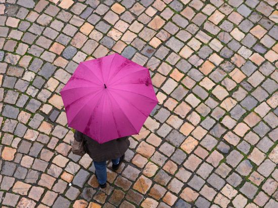 Eine Frau geht mit einem Regenschirm auf einer Straße entlang.