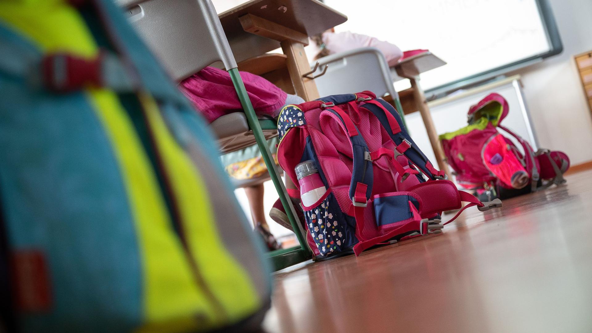Schulranzen stehen in einem Klassenraum auf dem Boden.