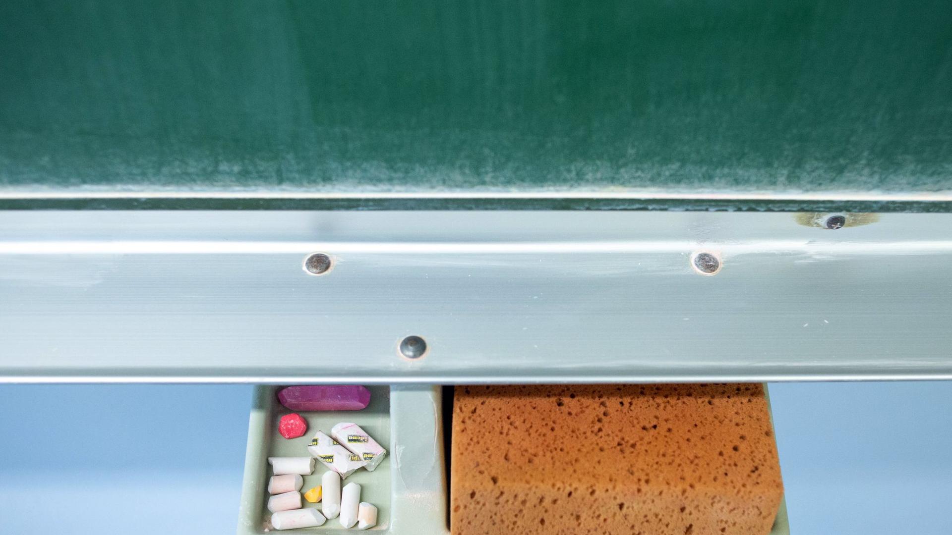 Schwamm und Kreide liegen in einem Klassenraum unter einer Tafel.