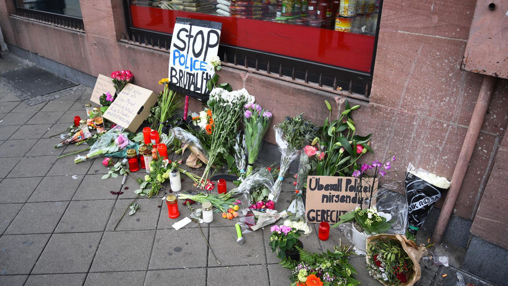 Blumen, Kerzen und Schilder liegen und stehen an dem Ort, an dem ein Mann nach einer Polizeikontrolle gestorben ist.