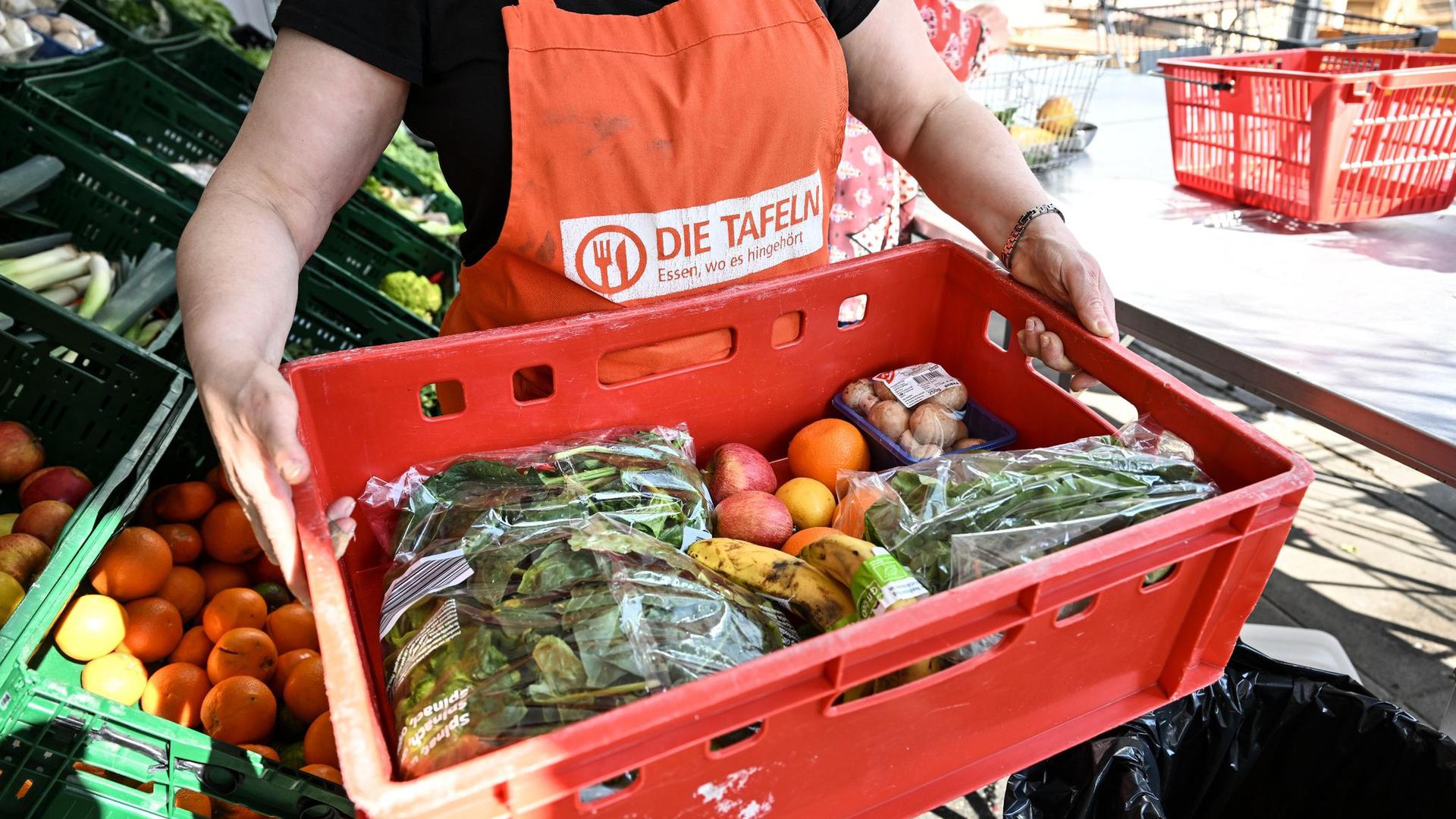 Eine Mitarbeiterin des Tafel-Ladens trägt eine Kiste voll mit Obst und Gemüse.