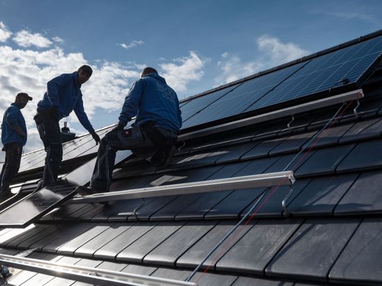 Mitarbeiter montieren Photovoltaikmodule auf dem Dach eines Gebäudes.