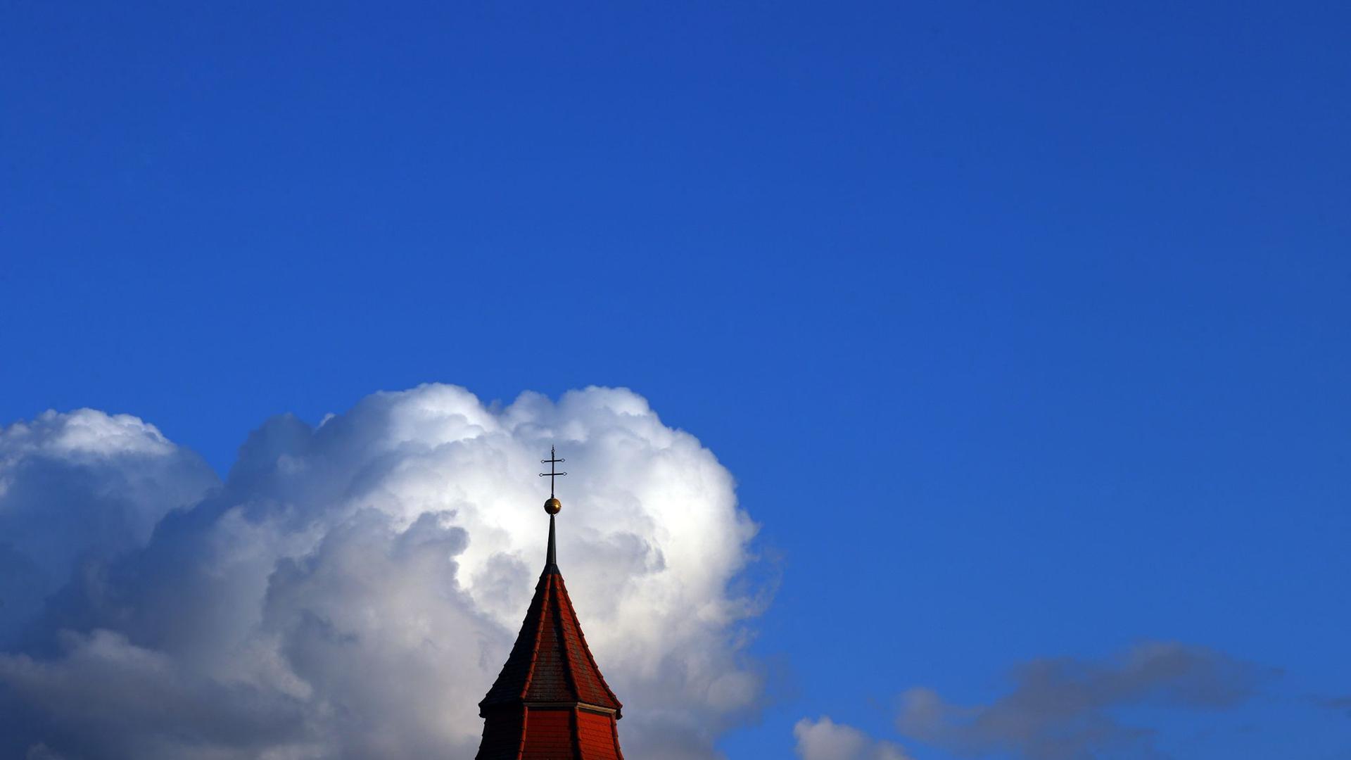 Wolken türmen sich hinter einem Kirchturm.