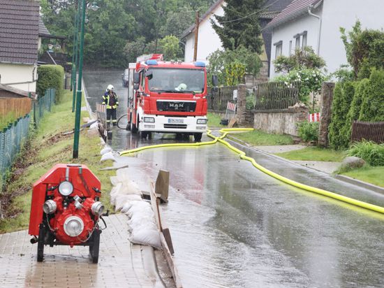 Feuerwehrleute haben auf einer Dorfstraße  nach heftigen Regenfällen Pumpen aufgestellt.
