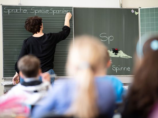 Eine Lehrerin schreibt in einer Grundschule Wörter, die mit „Sp“ beginnen, an eine Tafel.