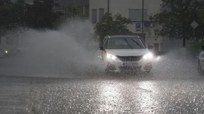 Ein Auto fährt bei starkem Regen auf einer überfluteten Straße.