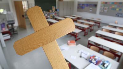 Ein Kreuz wird im Klassenzimmer einer Grundschule gehalten.