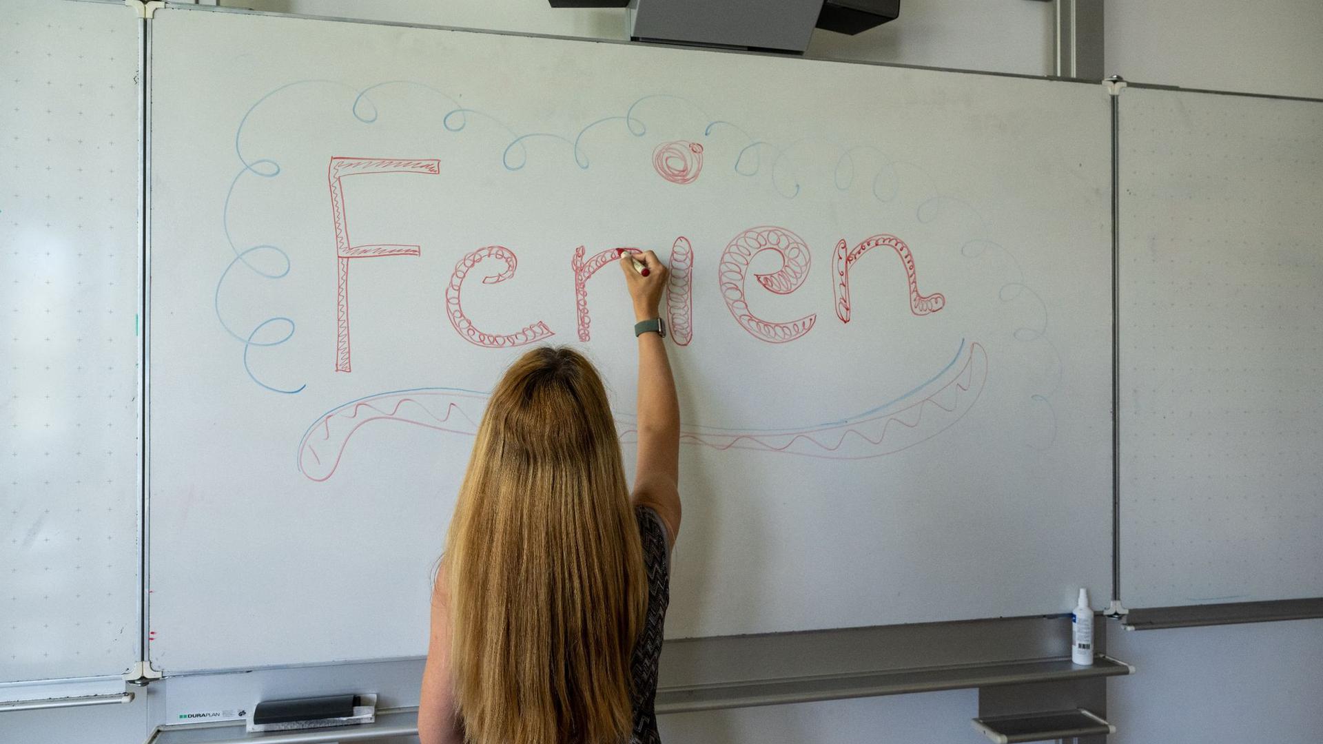 Eine Lehrerin schreibt das Wort „Ferien“ an eine Tafel.