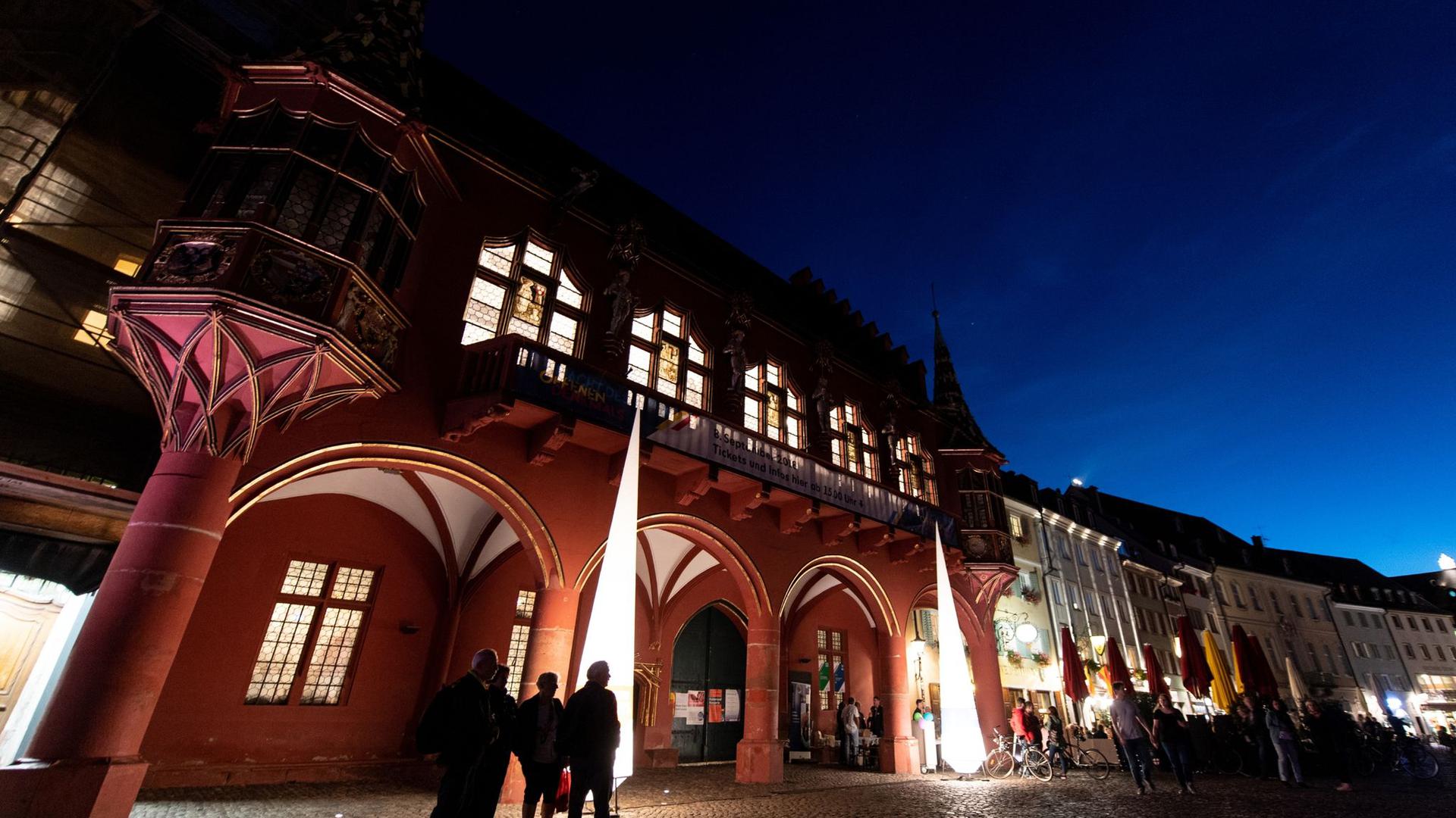 Menschen stehen während der Nacht des offenen Denkmals vor dem historischen Kaufhaus in Freiburg.