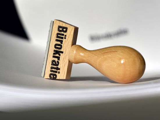 Ein Stempel mit der Aufschrift „Bürokratie“ liegt auf Papieren.