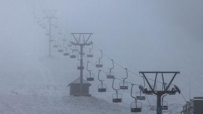 Liftgondeln hängen an einem Skilift, während darunter Schnee liegt.