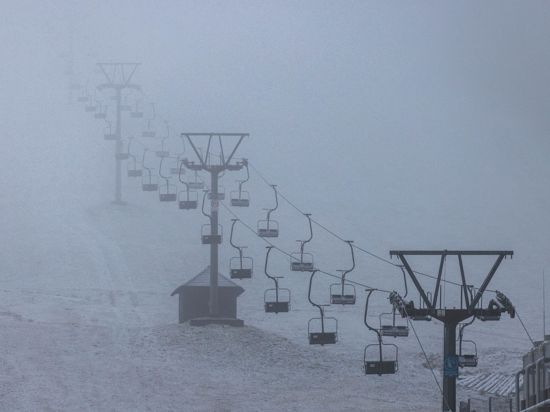 Liftgondeln hängen an einem Skilift, während darunter Schnee liegt.