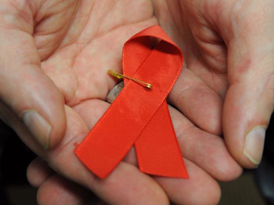 Ein Mann hält eine rote Schleife als Symbol der Solidarität mit HIV-Positiven und Aids-Kranken in den Händen.