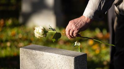 Ein Mann legt eine Rose auf einen Grabstein .