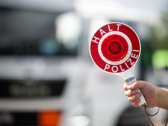 Ein Polizist hält bei einer Verkehrskontrolle eine Polizeikelle in der Hand.