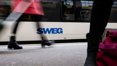 Menschen gehen an einem Zug mit dem Logo der SWEG vorbei.