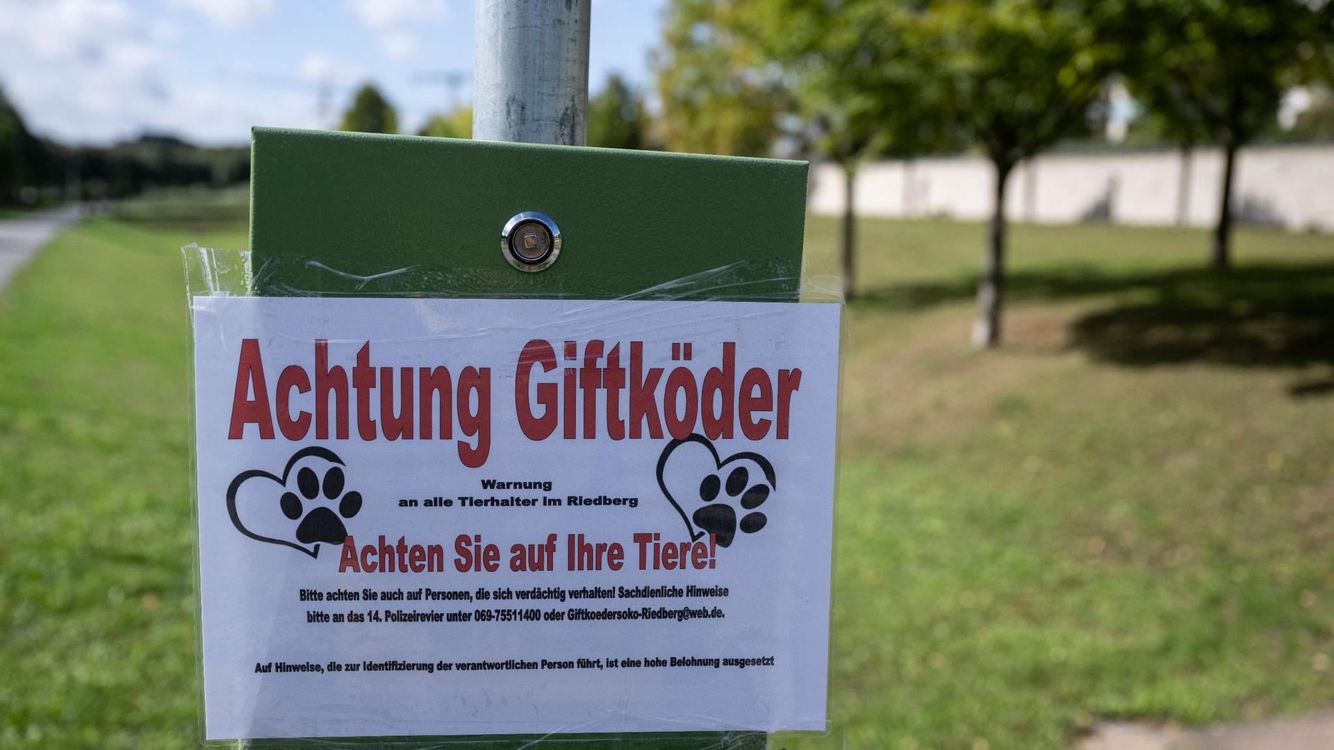 „Achtung Giftköder“ steht auf einem Schild am Rande einer Hundewiese in einem Stadtteil.