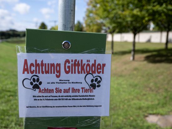 „Achtung Giftköder“ steht auf einem Schild am Rande einer Hundewiese in einem Stadtteil.