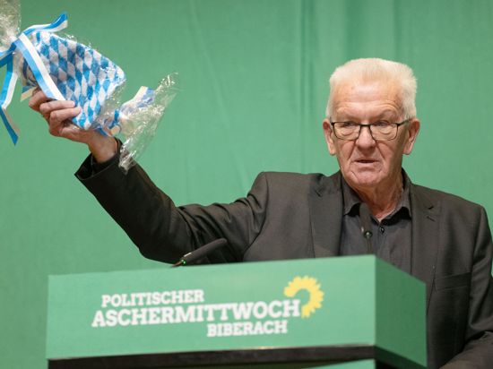 Baden-Württembergs Ministerpräsident Winfried Kretschmann zeigt in der Stadthalle einen Waschlappen.