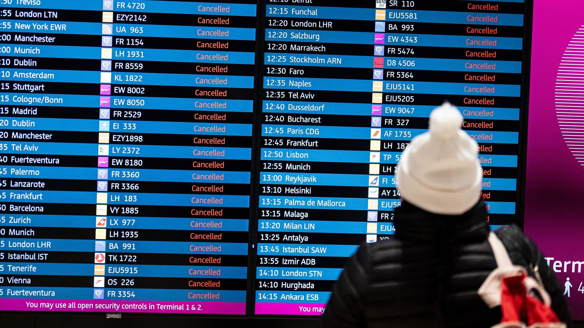 Eine Frau blickt an einem Flughafen auf eine Anzeigentafel mit gestrichenen Flügen.