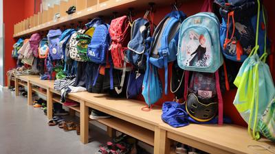Sporttaschen und Schulranzen hängen an der Garderobe vor einem Klassenzimmer.