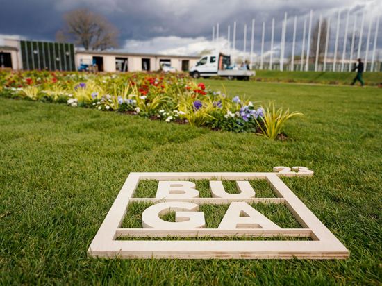 Ein Holzrahmen mit der Aufschrift „BUGA 23“ liegt auf dem Gelände der Bundesgartenschau vor einem Blumenbeet.