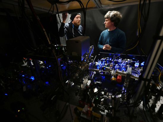 Florian Meinert (r), Gruppenleiter am 5. Physikalischen Institut der Universität Stuttgart, unterhält sich im Labor des Instituts hinter einem Neutralatom-Quantencomputeraufbau, an welchem an einem neuen Quantenbit-Konzept auf der Neutralatom-plattform geforscht wird, mit einem Doktoranden.
