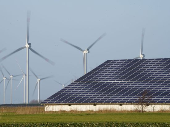 Windenergieanlagen stehen neben einer Halle mit Photovoltaik-Anlagen.