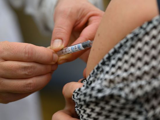 Ein Arzt impft eine Jugendliche gegen die Grippe.